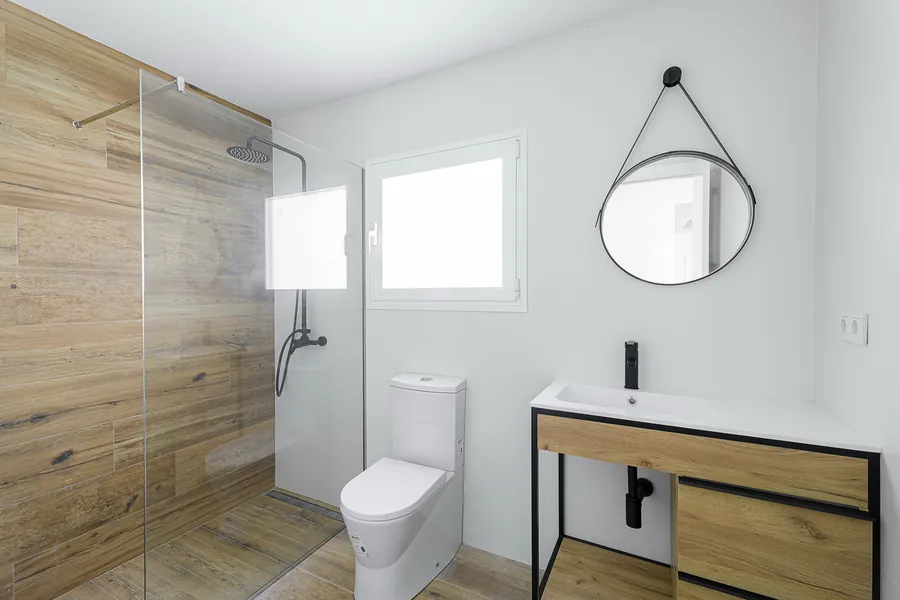 Baño con el revestimiento de madera en la ducha y el espejo circular