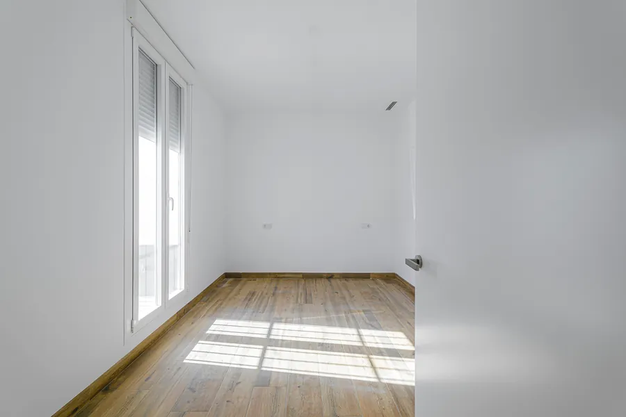 Segundo dormitorio, vacío, con el pavimento de madera iluminado por el sol